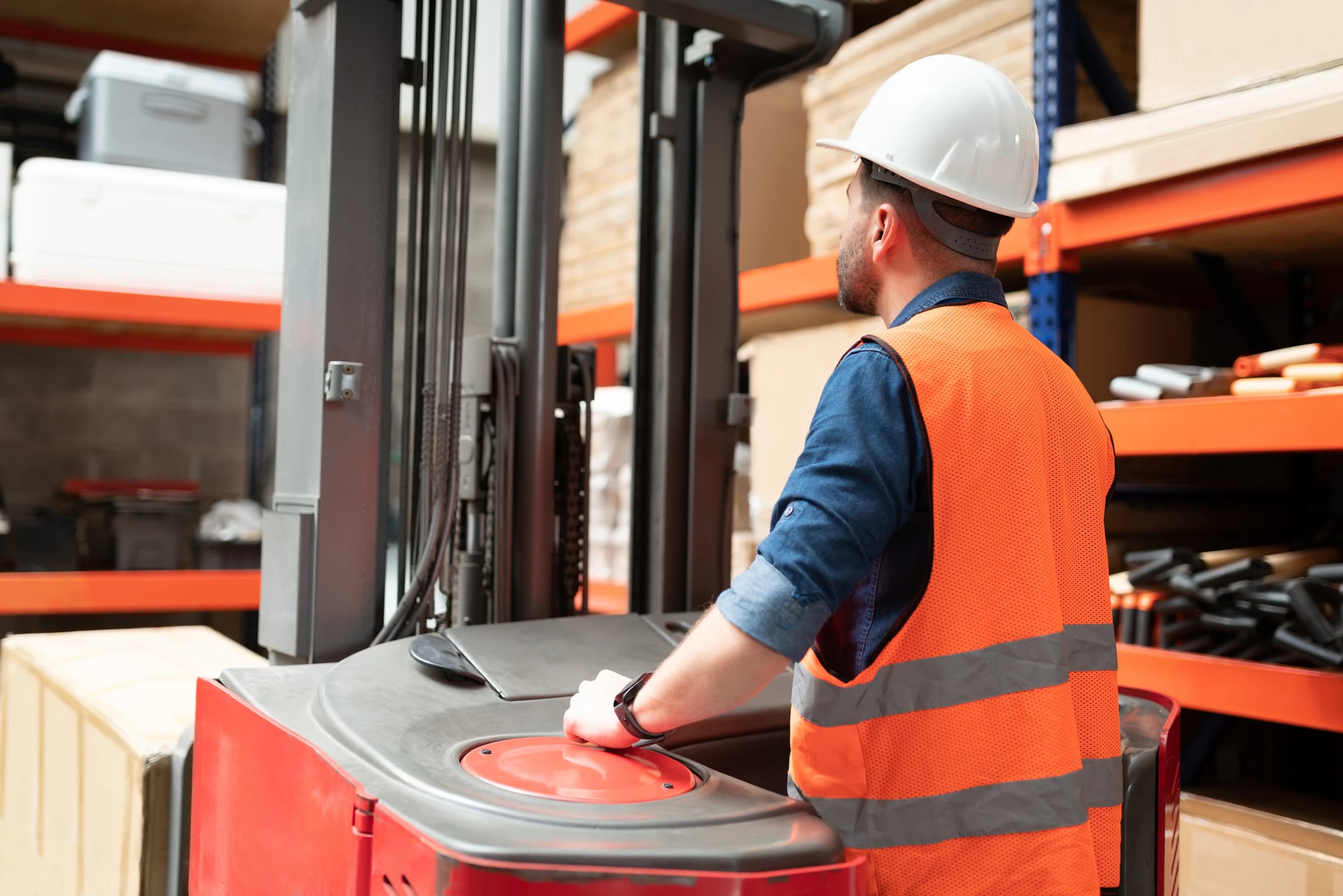 A warehouse worker operating a lift beside storage racks.